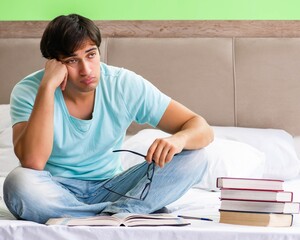 Student preparing for exams at home in bedroom sitting on the be