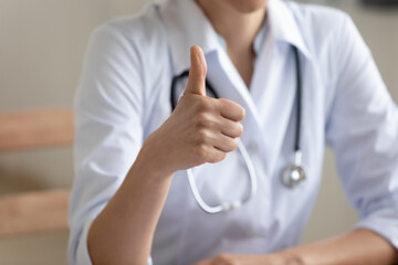 Crop close up of female doctor or GP in white medical uniform show thumb up recommend good quality medical service, woman nurse or physician give recommendation to healthcare system in hospital