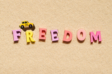 Toy yellow taxi car ride on the colorful letters of word freedom on beach sand. Concept. Fast and...