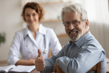 Smiling mature male patient sit at consultation with doctor in clinic show thumb up recommend good...