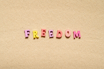 Colorful freedom word made from  letters on the sand beach. Travel relaxation concept. Creative