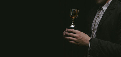 Businessman holding gold trophy on dark background