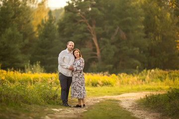 Fototapeta premium A young pregnant woman and her husband are embracing while standing in a forest clearing. Image with selective focus.