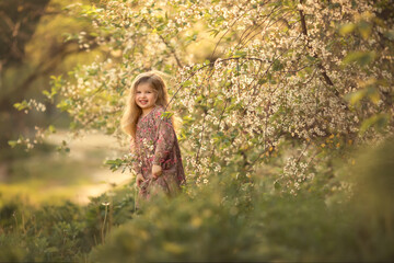 A little girl stands next to a large blooming spring tree. Image with selective focus.