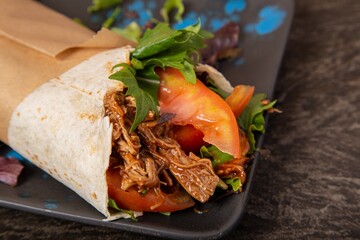 Closeup shot of a juicy tortilla wrap with pulled meat, tomatoes, and greens