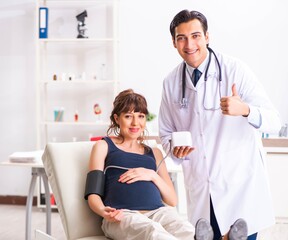 Fototapeta premium Young doctor checking pregnant woman's blood pressure