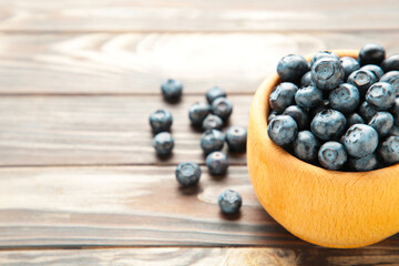 Blueberries in a bowl on brown wooden table with copy space.