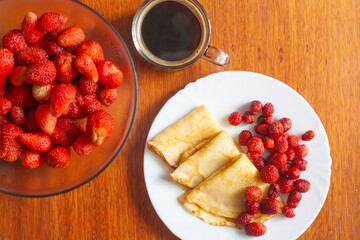 Breakfast, pancakes with berries, coffee and a bowl of berries on a wooden table
