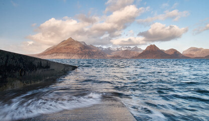 The black and red cuillin mountains of isle of sky from Elgol in the late afternoon sun clouds over mountains as sea waves blur up the slipway