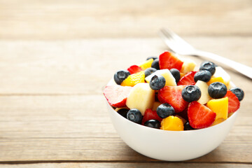 Fruit salad in a bowl with fork, served on grey background.