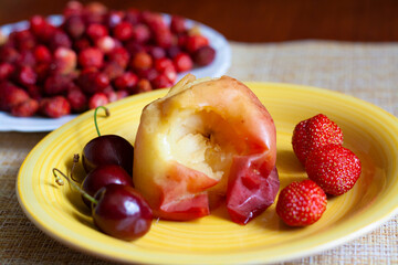 Fruit dessert, baked apple, cherry and strawberry on a yellow plate, strawberry on a blue plate in the background