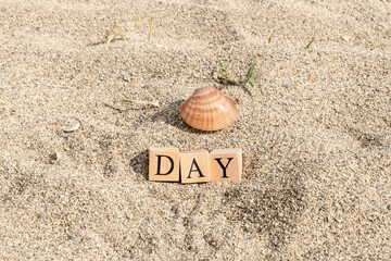 Day word made of wooden cubes. Close-up on the beach sand.