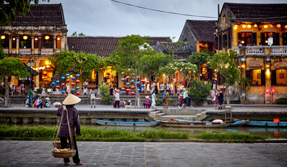 Vietnam Hoi An loan person in rice hat looking across water to colorful lanterns and old buildings with restaurants  © GrahamForresterPhoto