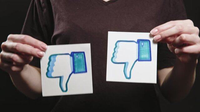 Kharkiv, Ukraine - May 12, 2020: Dislike logo. Negative feedback. Social media unlike. Woman hands disapproving post with thumb down icons.