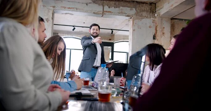 Confident handsome young Caucasian coach businessman motivating multiethnic team at modern office meeting slow motion.
