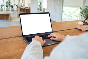 Fototapeta premium Mockup image of a woman using and typing on laptop computer keyboard with blank white desktop screen on wooden table