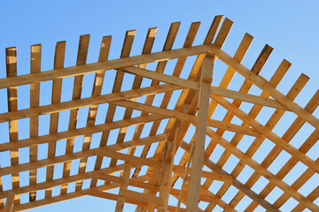 Yellow wooden rafters against the blue sky. Bright background on the topic of construction and...