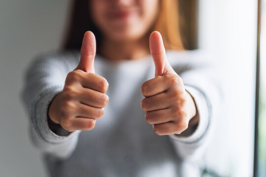 Closeup image of a young woman making and showing thumbs up hand sign