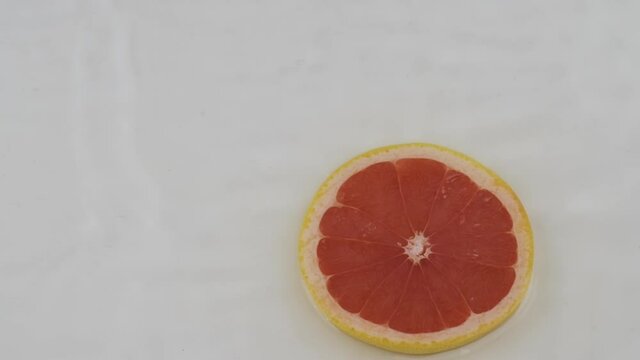 Fall of red slice of grapefruit, pomelo in white water. Slow motion.