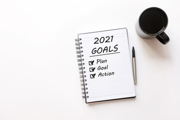 Flat lay of Notebook with text written '2021 Goals'  Plan, Goal, Action, a pen and coffee on white isolated background. New Year Resolution concept