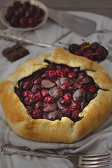 Dark chocolate and sour cherry galette crusty pie in a dark and moody atmosphere surrounded by cherries and vintage silverware
