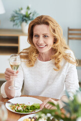 Vertical portrait of elegant mature woman raising champagne glass while enjoying romantic dinner