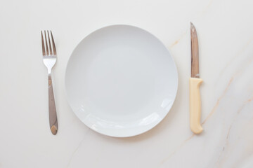  Empty white plate with cutlery on a marble table, saucer, fork and knife. The concept of diet, fasting