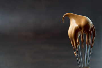 Whisk with fluffy creamy whipped coffee foam on a dark background. Trendy food and drink concept. Copy space.