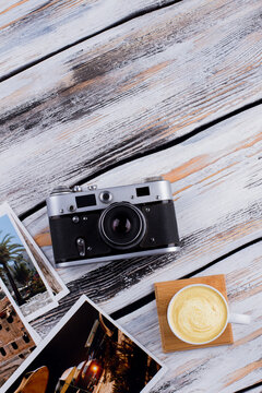 Cup of cappuccino and vintage photo camera with photos. Flat lay top view. White wooden background.