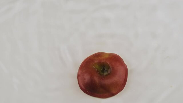 Fall of red slice of apple in white water. Slow motion.