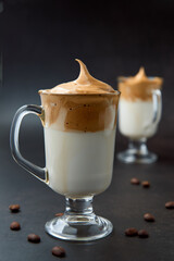 Glasses of trendy fluffy creamy dalgona or whipped instant coffee with milk and coffee beans on the dark background. New popular food and drink trend concept. Copy space.