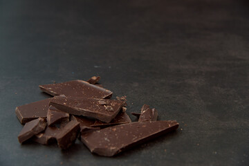Dark chocolate stack, chips and cocoa powder on a dark background. Confectionery and food concept. Top view, copy space, selective focus.