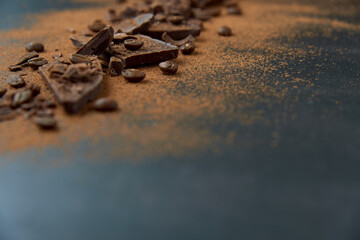Dark chocolate stack, chips and cocoa powder with coffee beans on a dark background. Confectionery and food concept. Top view, copy space, selective focus.