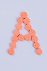 The letter A made fo round pills. Orange drugs in a shape of a letter isolated on o white background.