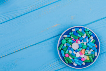 Topview plate with heap of pills. Blue wooden table on the background.