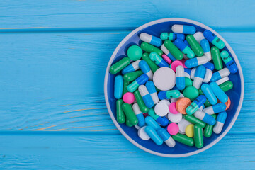 Flat lay plate full of various pills. Blue wood on background.