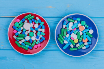 Two plates filled with pills. Topview flat lay. Blue wooden background.