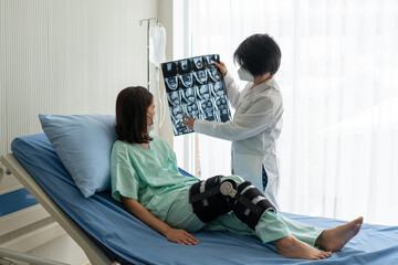 orthopedist shows magnetic resonance imaging or MRI of knee to asian patient that has knee injury...