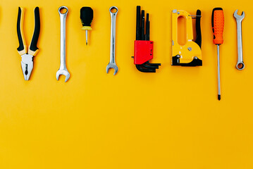 Tools top view on yellow background. Plier, open wrenches, screwdrivers and staple gun flat lay...