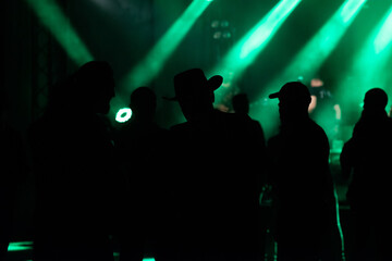 Blurred image of silhouette of raised arms, crowd of people in the front of bright stage lights at rock festival