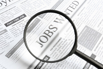 Looking through magnifying glass at newspaper, closeup. Job search concept