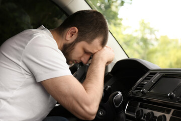 Tired man sleeping on steering wheel in his car