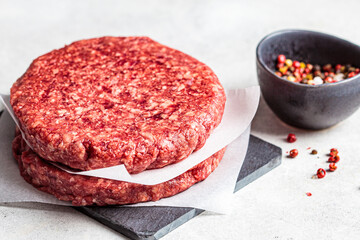 Raw burger patties on slate board, white background.
