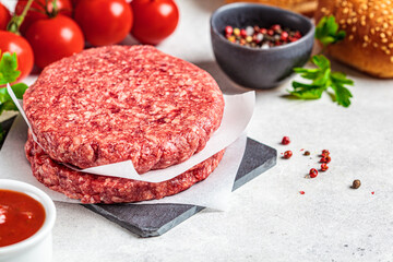 Raw burger patties on slate board, white background.