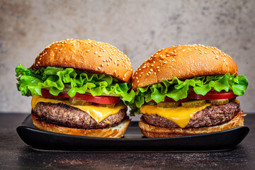 Homemade beef burgers with cheese, pickles and vegetables, dark background.