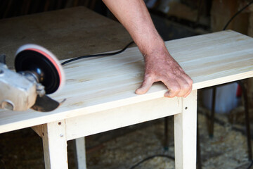 a worker using a sanding machine works with wood in a carpenter's workshop