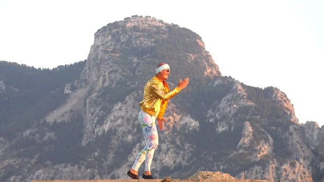 Young bald slender freak man caucasian in tight leggings, gold jacket, bandage on his head, dancing on roof at sunset, runs, has fun, behaves unusually. Slow motion video. Fun, humor, unusual people