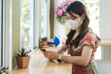 Asian woman wearing protective face mask and using smartphone in restaurant, protect coronavirus...