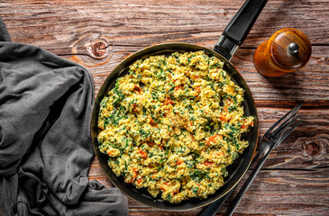 scrambled eggs with spinach and tomato in pan on wooden table background