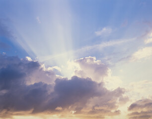 Sun rays coming out from behind clouds with blue sky above